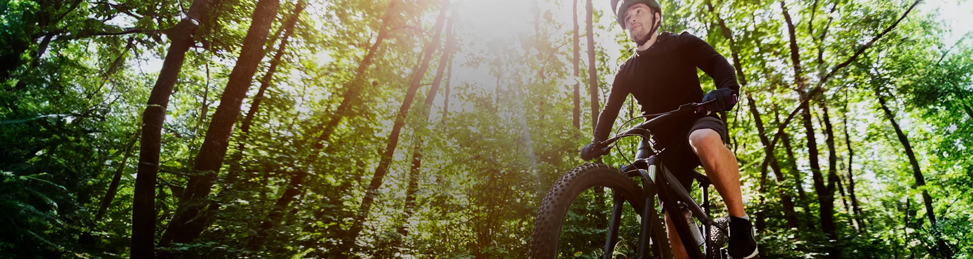 Homem parado com a bicicleta em meio a natureza segurando o celular
